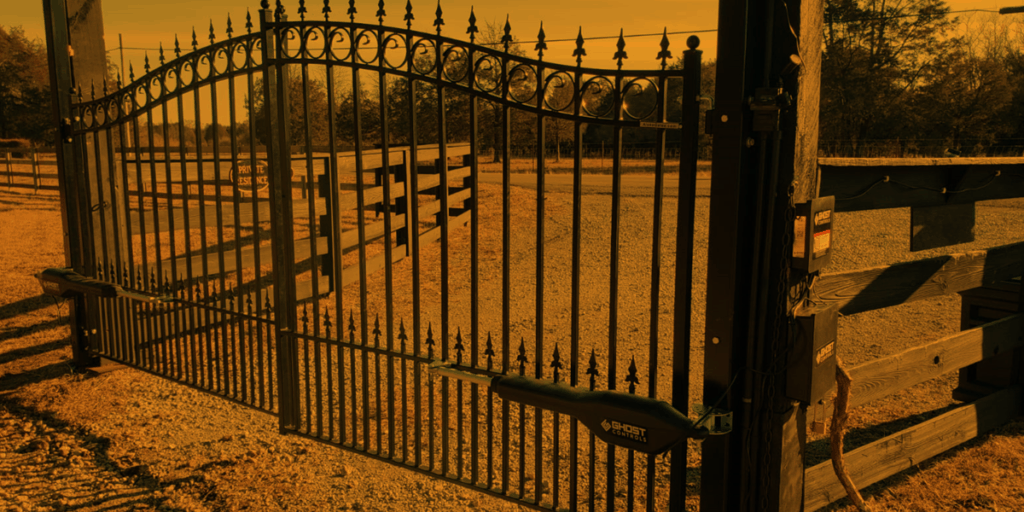 Orange-tinted automated iron driveway gate installed by EVERLAST GATES & FENCE.