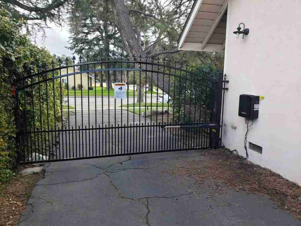 EVERLAST GATES & FENCE automatic wrought iron driveway gate with swing operator arm.