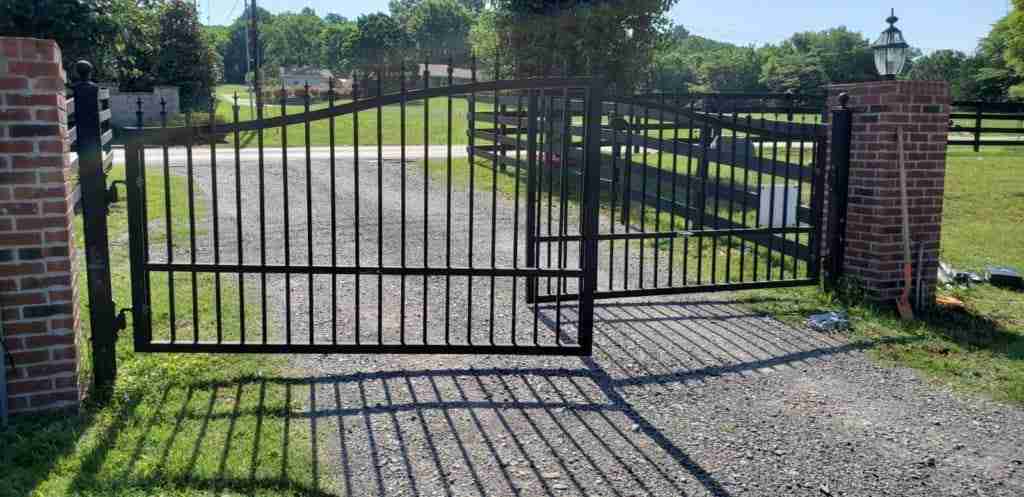 EVERLAST GATES & FENCE black metal driveway gate across a gravel entrance.