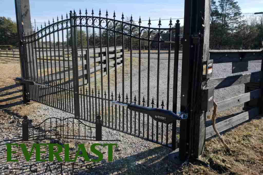 Automated wrought-iron driveway gate with motor arm and Everlast Gates logo.