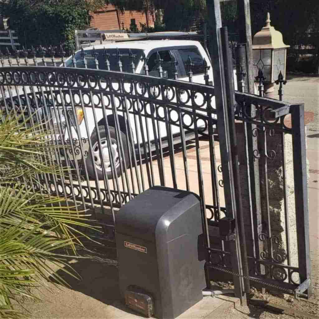 Automatic gate opener installed on black wrought iron sliding driveway gate.