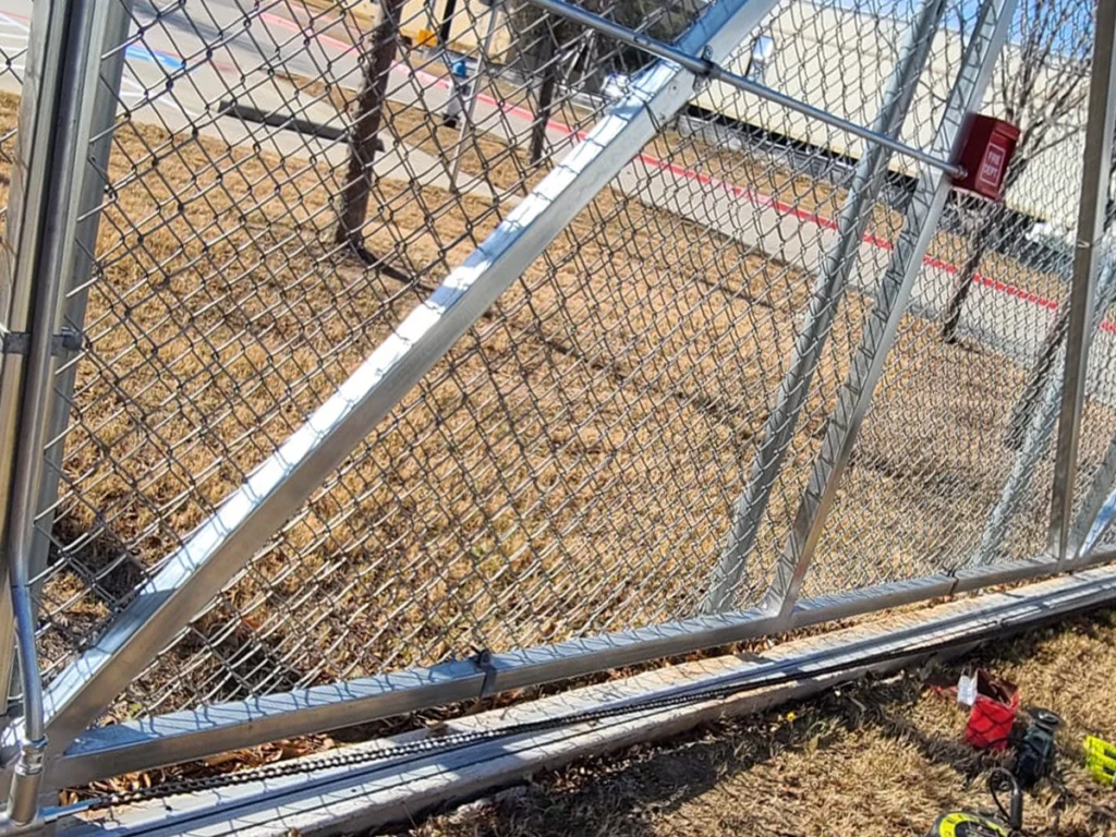 echnician fixing a commercial gate in Carrollton, TX with Everlast Gates & Fence logo visible.