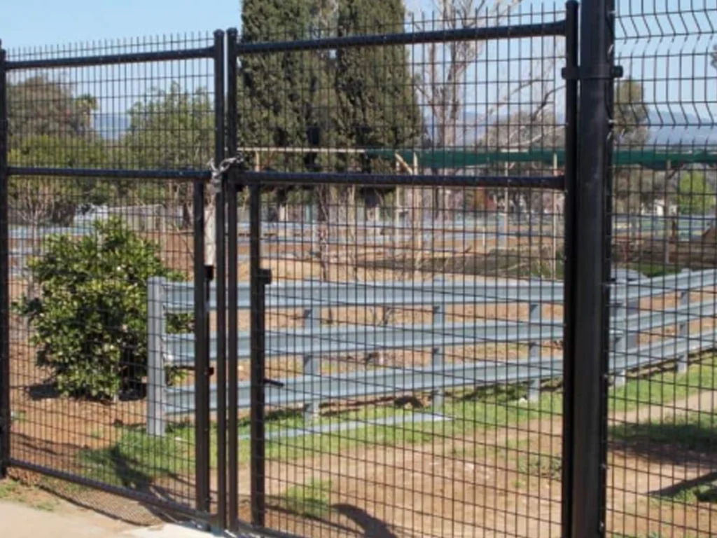 Gate and chain-link fence opening into a fenced park with blue bleachers visible in the background