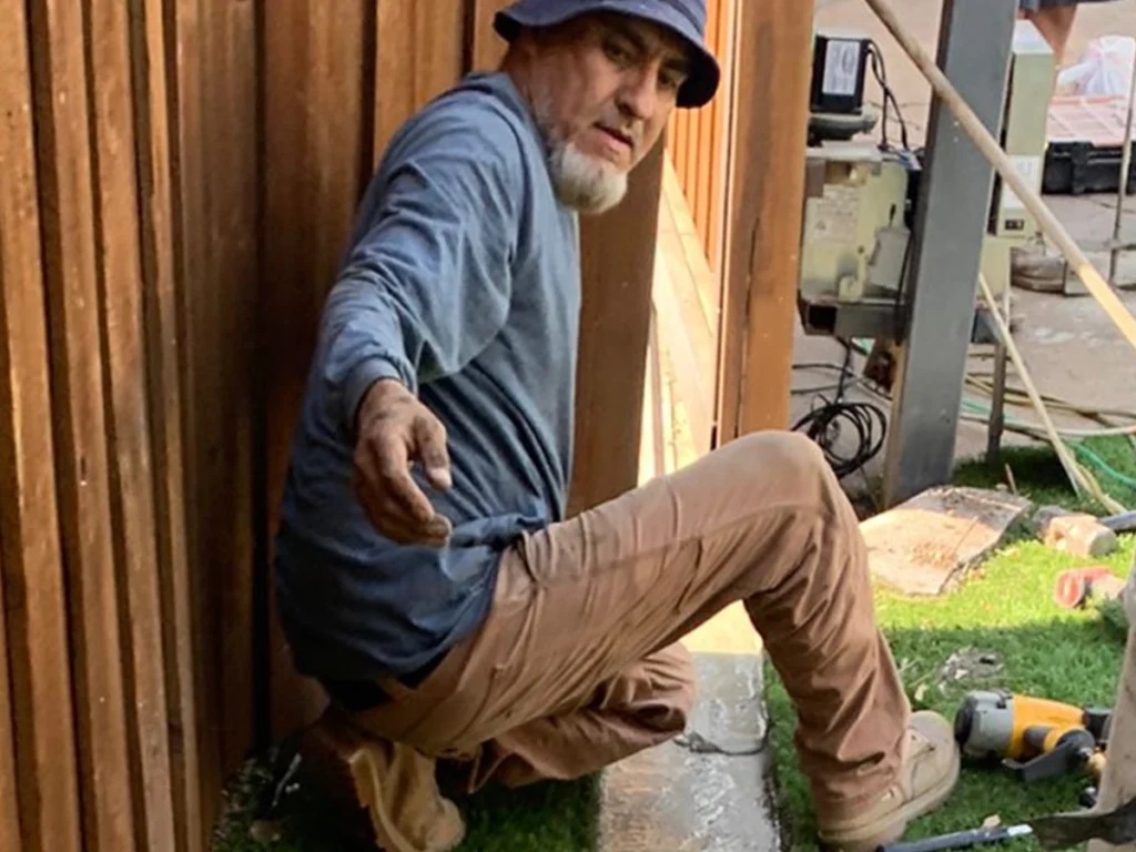Homeowner inspecting a wooden gate in Garland, Texas during summer for maintenance
